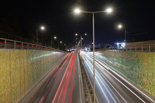 View of long-exposure vehicle light trails along Triq Mikiel Anton Vassalli, a sunken arterial road in Msida, Malta, lined with tiled retaining walls and streetlights at night.