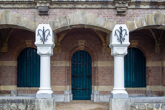 View of the historic brick architecture at Naarden-Vesting, featuring an arched doorway, white columns with decorative metalwork, and green shutters in Naarden, Noord-Holland, Netherlands.