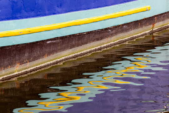 View of the colorful painted hull of a boat reflecting in the calm water of a canal in Amsterdam, North Holland, Netherlands.