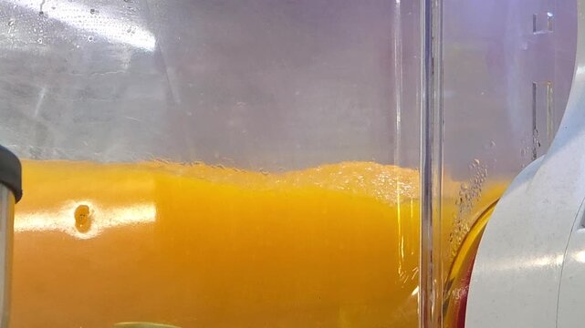 Automatic cold juice dispenser machine mixing and cooling fresh orange drink inside clear plastic tank