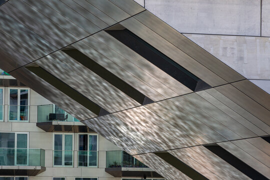 View of the metallic, angled facade of the Sluishuis building with light reflections and residential balconies in the background in Amsterdam, North Holland, Netherlands.