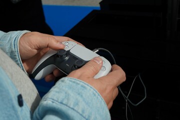 Close-up of hands using a wired game controller against a dark blue background. Selective focus highlights the controller and fingers during video gaming and digital entertainment. © Dr. CraftLab