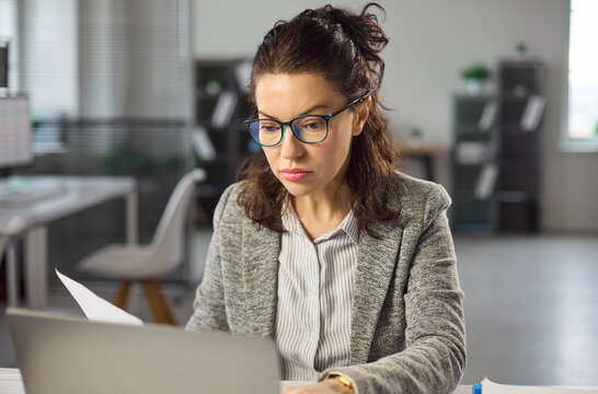 Analyst woman with laptop in office reviewing document. She checks finance data, validates entries and paperwork and prepares a report for planning, budget. Clear business analysis concept.