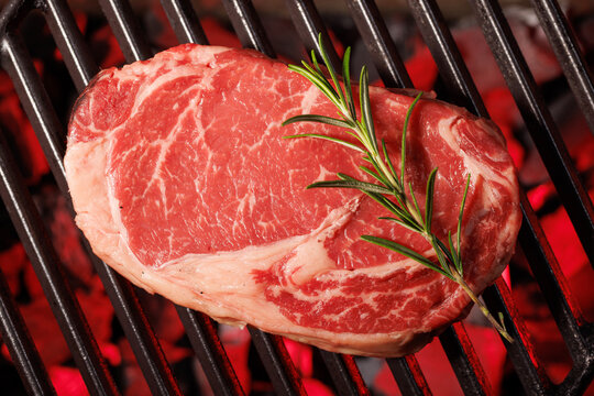 Raw ribeye steak with rosemary on barbecue