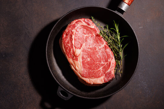 Raw marbled ribeye in skillet with herbs