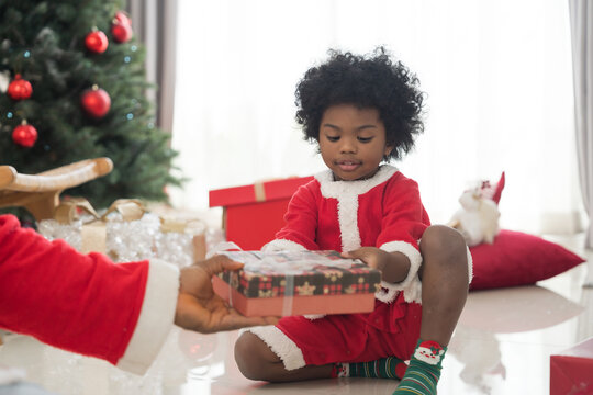 African American father celebrates Christmas and give Christmas gift box to little son in festive living room. Happy cute African American little boy with Chirstmas gift box