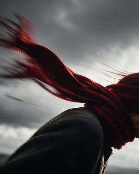 Dynamic blur of a red knit scarf whipping in freezing autumn winds, expressing the wild energy between person and autumn elements.