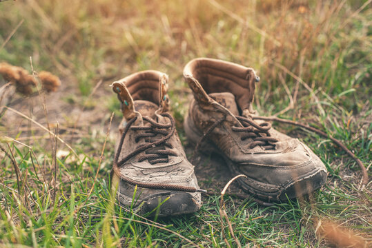 Pair of old worn shabby shoes with dusty cracked leather and untied laces standing in dry grass