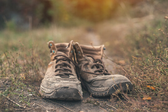 Pair of old worn shabby shoes with dusty cracked leather and untied laces standing in dry grass