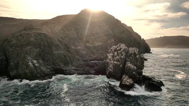 Aerial view of ocean waves crashing on rocky cliffs at sunset