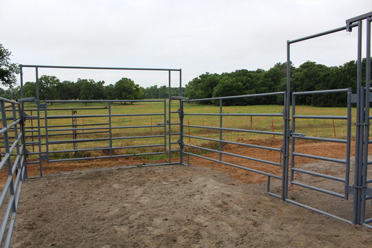 Empty gray pipe corral with walk through gate frames beside a meadow