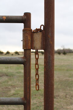 Rusty hinge and hanging chain on a steel gate post in a field