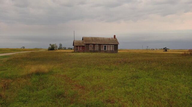 Abandoned wooden farmhouse in rural prairie landscape under cloudy sky