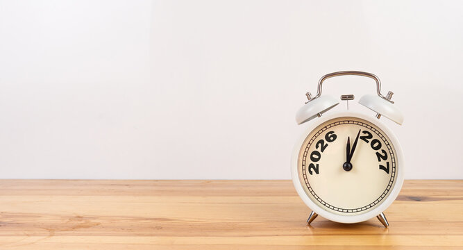 Alarm clock showing 2026 replaced by 2027 text written on wood table white background.
Good bye 2026 - 2027 happy New Year coming concept.