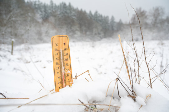 Thermometer in snow covered landscape, cold frosty weather forecast in winter, measure the temperature, ice, frost and snowy meadow