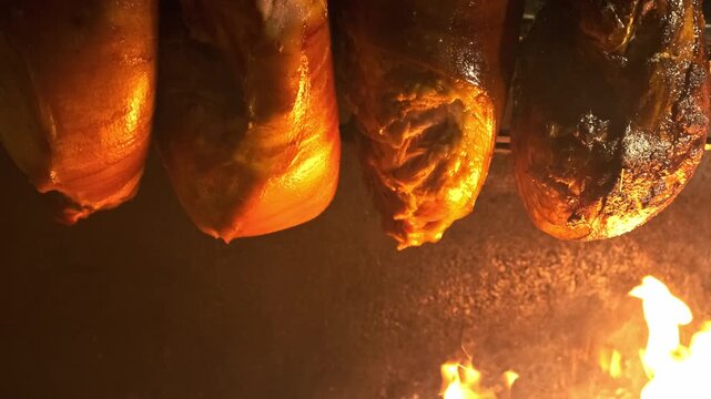 juicy pork hocks roasting over an open wood fire on a rotisserie. Melted fat drips down to glowing flames. Christmas market food stand