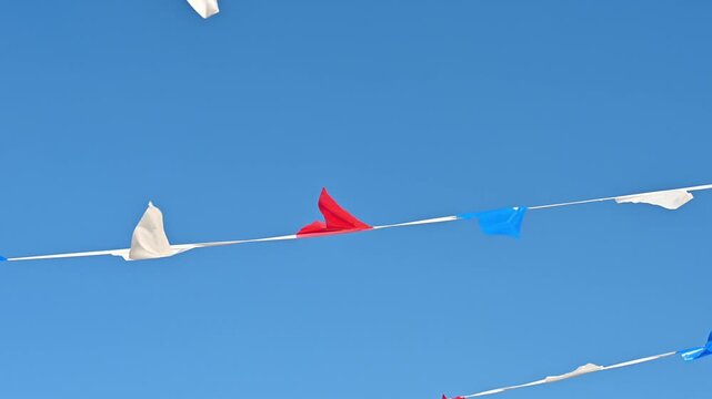 A video of red, white, and blue bunting flags fluttering on strings against a clear blue sky.