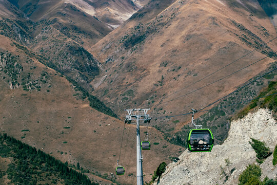 View of a green cable car carrying passengers over the rugged, dry mountain slopes of Ala Archa National Park in Bishkek, Chuy Region, Kyrgyzstan.