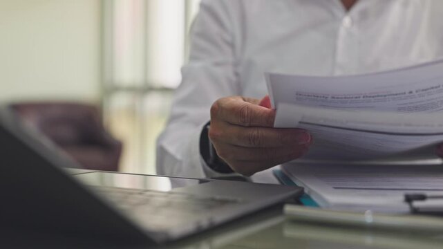 Investor reviews earnings report alongside open laptop computer inside modern corporate office. Financial document analysis, shareholder yield metrics audit, investment strategy planning.