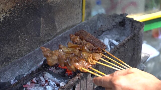 Traditional Indonesian satay kere skewered on bamboo sticks grilled over hot charcoal on street food vendor grill, authentic local culinary delicacy from Solo Central Java full of savory taste.