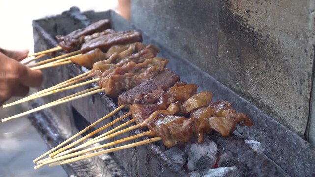 Traditional Indonesian satay kere skewered on bamboo sticks grilled over hot charcoal on street food vendor grill, authentic local culinary delicacy from Solo Central Java full of savory taste.