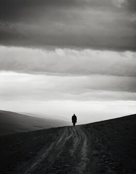 Solitary person walking on remote dirt road under cloudy sky
