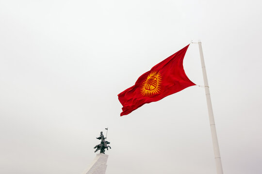 View of the national flag of Kyrgyzstan waving in the wind above the Manas statue in Bishkek, Bishkek City, Kyrgyzstan.