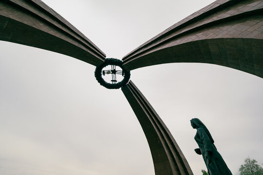 View of the Victory Monument with its three curved arches and central wreath, featuring a bronze statue of a woman standing in front, Bishkek, Bishkek City, Kyrgyzstan.