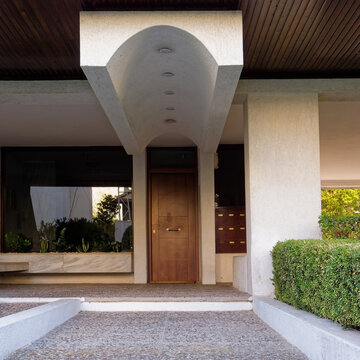 view of a modernist Athenian apartment building entrance showing the vaulted canopy, wooden door, and pebbled steps in Athens, Greece.