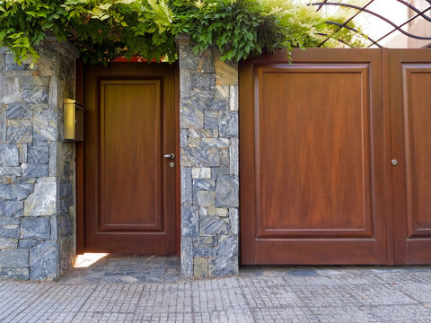 Exterior view of a private residential wooden pedestrian door and garage gate set into a stone fence in Athens, Greece.