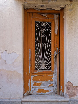 Vertical view of a locked old orange wooden door with art deco ironwork and peeling paint in Athens, Greece.
