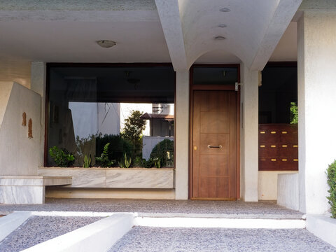 Detailed architectural photograph highlighting the geometric curves of an arched concrete canopy, glass reflections, and wood door textures.