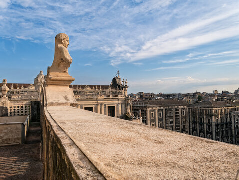 Terrace balustrade with stone bust sculpture overlooking historic Catania city buildings from Badia di Sant'Agata in Sicily, Italy.