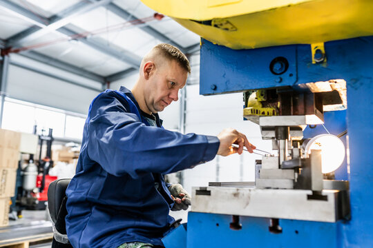 Blue collar factory worker operating mechanical stamping press and handling workpieces. Hands-on production work in metalworking workshop