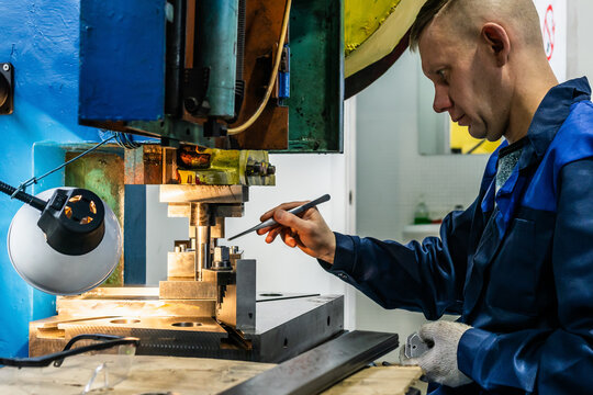 Metal component production with press operator bending blanks on stamping press. Blue collar employment in industrial metalworking, medium shot