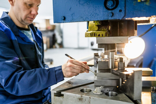 Press operator manufacturing metal parts on mechanical stamping press. Close-up of blue collar work in metalworking shop