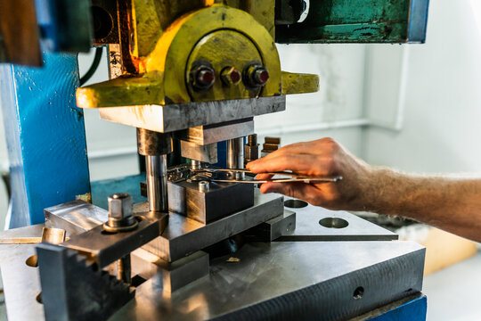Blue collar factory worker operating mechanical stamping press and handling workpieces. Hands-on production work in metalworking workshop