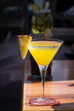 Vibrant yellow tropical martini cocktail garnished with a pineapple wedge on a wooden table.