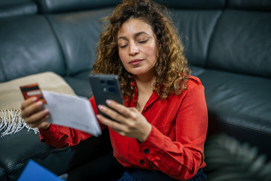 Woman comparing credit card details with smartphone screen at home