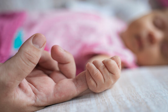 Little baby holding adult finger while sleeping