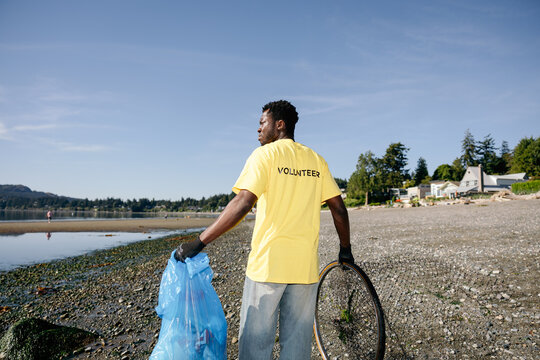 Volunteer cleaning beach shoreline with trash bag and tire