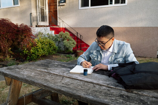 Student writing notes outdoors at a picnic table, candid focused