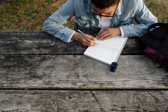 Candid student sketching outdoors on a weathered wooden bench