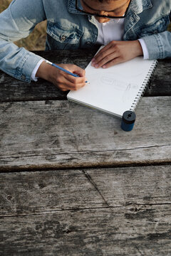 Man sketching in notebook outdoors on rustic wooden table