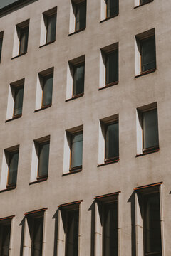View of the facade of a modern building in Helsinki, featuring uniform rows of rectangular windows and sharp shadows cast on the light-colored wall, Helsinki, Uusimaa, Finland.