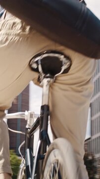 Man with helmet and crossbody bag cycles past office buildings