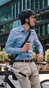 Man drinks coffee leaning on bicycle in glass office courtyard