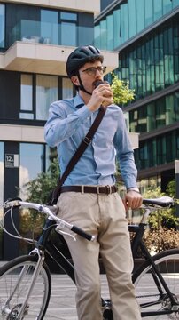Man waits leaning on bicycle with coffee cup by office building