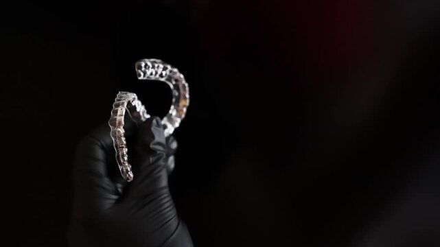 Black-gloved hand displaying a clear dental retainer on a dark backdrop