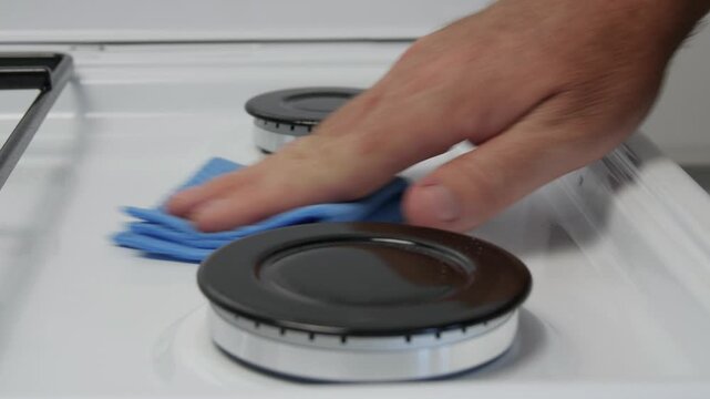 Man Cleaning the Gas Cooker with a Clean Wipe and Cleaning Solution. Daily Household Chores in the Kitchen.